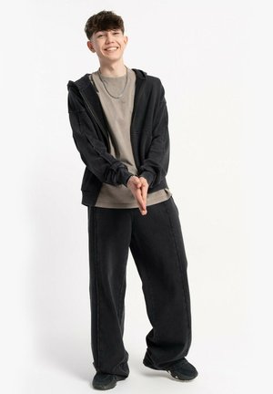 Czarna bluza z suwakiem na szaro, z szarym t-shirtem, w połączeniu z luźnymi czarnymi spodniami i ciemnymi butami. Akcesoria to łańcuszek i bransoletka.