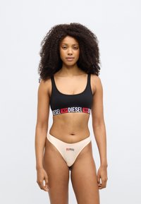 Fekete sportmelltartó piros és fehér "DIESEL" logós szalaggal; bézs tangával párosítva, amely hasonló logóval van ellátva. Végig sima anyagtextúra.