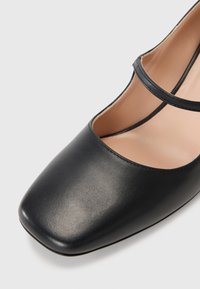 Black leather shoe with a square toe, featuring two thin straps across the top and a smooth finish with a light inner lining.