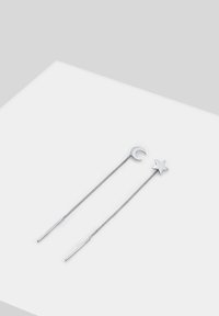 Fermagli in argento con un design a mezzaluna e stella, dotati di catene sottili e punte dritte, che mostrano un aspetto elegante e minimalista.