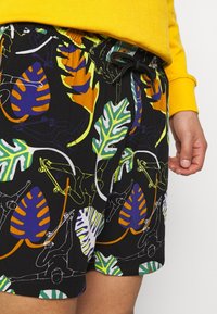 Shorts de bain noirs avec des motifs colorés de feuilles et de skate, taille élastique avec cordon de serrage, et texture de tissu lisse.