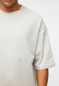 T-shirt surdimensionné gris clair en coton doux, avec un col rond et des manches courtes, offrant une texture lisse et une coupe décontractée.