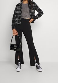 Musta ja valkoinen ruudullinen takki, harmaa ribattua kangasta crop-top, mustat levenevät housut sivukiiltoilla, musta käsilaukku ja mustavalkoiset sneakerit.