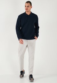 Polo shirt bleumarin cu mânecă lungă, dintr-un material texturat, cu sistem de închidere cu trei butoane, asortat cu pantaloni bej deschis, eleganți și adidași închiși la culoare.