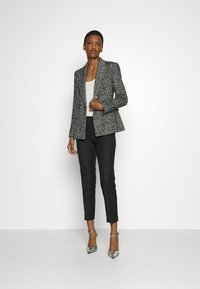 Black and white textured blazer with a tailored fit, worn over a white top, paired with black tailored trousers and silver high-heeled shoes.