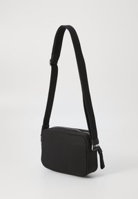 Black rectangular bag made of textured fabric, featuring a zip closure and a flat adjustable strap. Minimalist design with no visible hardware details.