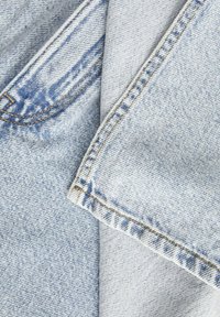 Világoskék farmeranyag, ami egy világosabb árnyalattal van rétegezve, látható varrással és enyhén texturált felülettel.
