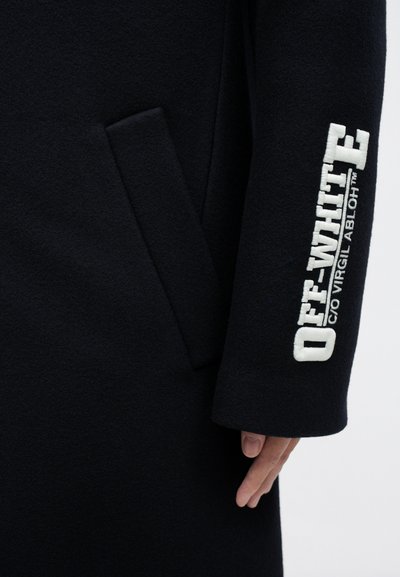 Černý vlněný kabát s přední kapsou a vyšívaným textem "OFF-WHITE" v bílé barvě na rukávu. Hladká textura a přiléhavý střih.