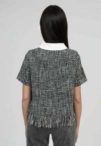 T-shirt à manches courtes en tissu texturé noir et blanc, avec un ourlet frangé et un col blanc. Le matériau semble tissé avec un motif subtil.