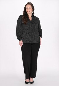 Schwarze Bluse mit weißen Punkten, V-Ausschnitt, lange Ärmel. Kombiniert mit schwarzen weiten Hosen und schwarzen hohen Schuhen. Dezenter Fall und Glanz.