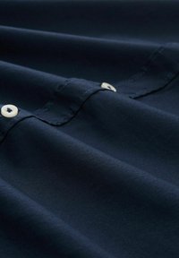 Navy stof met een zachte textuur, voorzien van ronde naden en crème-kleurige knopen, gerangschikt in zachte plooien.