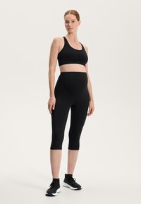 Črn športni modrček in visoko pasne legice iz raztegljive tkanine. Legice so skrajšane do sredine meč in so vse skupaj usklajene s črnimi supergami.