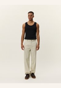 Black cotton tank top paired with cream-colored wide-leg trousers and brown lace-up shoes. The model stands upright against a neutral background.