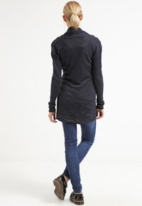 Námořnický pletený dlouhý kardigan s texturovaným lemem, spárovaný s modrými skinny džínami. Obsahuje šálový límec a přiléhavé rukávy.