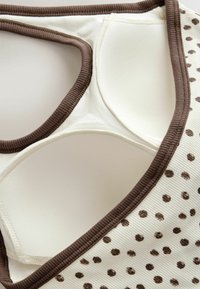 Gros plan d'un soutien-gorge en tissu crème avec bordure marron et pois marron, doté de bonnets rembourrés et de matériau doux texturé.