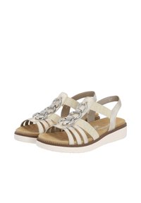 Sandali beige con un design a cinghie incrociate, caratterizzati da una grande catena metallica decorativa, una morbida soletta imbottita e una suola bianca.