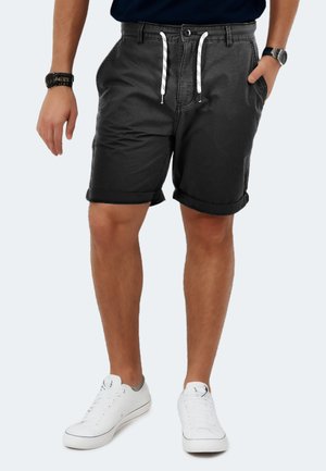 Schwarze Stoffshorts mit umgeschlagenen Säumen, vorderen Taschen und weißen Kordeln. Kombiniert mit weißen Sneakern und einem maritimen Hemd.