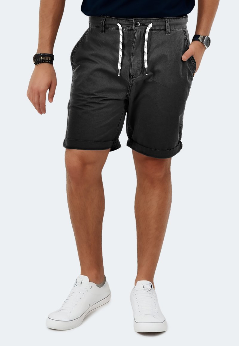 Schwarze Stoffshorts mit umgeschlagenen Säumen, vorderen Taschen und weißen Kordeln. Kombiniert mit weißen Sneakern und einem maritimen Hemd.
