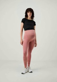 Leggings per gravidanza in morbido e elastico tessuto rosa, abbinati a una maglietta nera corta e a delle sneakers bianche. Texture liscia, design aderente.
