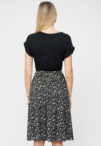 Top nero a maniche corte con maniche arrotolate, abbinato a una gonna a lunghezza ginocchio con stampa floreale, caratterizzata da uno sfondo nero e piccoli fiori multicolori.