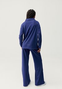 Námořnický modrý set domácího oblečení obsahující košilový top s dlouhým rukávem a široké kalhoty z jemné, hladké látky. Diskrétní značka na zadní straně.