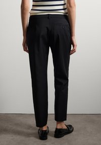 Pantaloni neri su misura con vestibilità slim, dotati di tasca posteriore e piega sottile, abbinati a scarpe nere, visti da dietro.