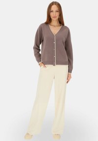 Cardigan w stonowanym lawendowym kolorze, wykonany z miękkiego materiału, z dekoltem w serek, długimi rękawami oraz guzikami przypominającymi perły. W zestawieniu z szerokimi kremowymi spodniami.