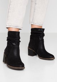 Botines negros de cuero con un diseño arrugado, que presentan una puntera redonda, tacón cuadrado y acentos texturizados en contraste.