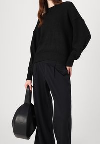 Schwarzer Strickpullover mit lockerer Passform und geripptem Saum, kombiniert mit schwarzen weiten Hosen und einer strukturierten schwarzen Handtasche.