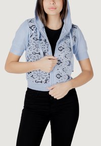 Sudadera cropped azul claro con encaje, mangas cortas, cremallera frontal y capucha con cordón. Top negro acanalado debajo y pantalones negros.