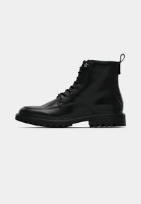 Črni usnjeni gležnjarji z gladkim zaključkom, okroglim sprednjim delom, modelom z zavezovanjem in robustnim gumijastim podplatom. Imajo zankico na zadnjem delu.