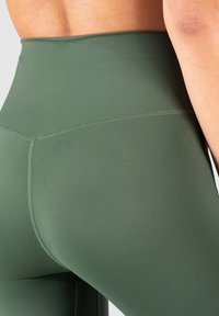 Leggings a vita alta in verde scuro, realizzati in materiale liscio e elastico. Presentano cuciture piatte e un design aderente per comfort e supporto.