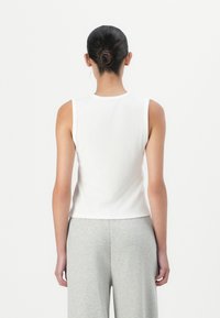 White, sleeveless top with ribbed texture and round neckline, paired with light gray, loose-fitting pants. Simple and minimal design.