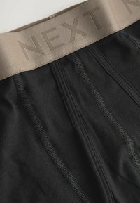 Fekete boxernadrág bézs elasztikus derékkal. A derékpánt kiemelkedő varrással rendelkezik, melyen a "NEXT" felirat látható. Puha pamut anyag látható.