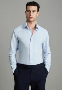 Hellblaues Langarmhemd mit Kragen, ausgestattet mit vorderen Knöpfen und einer glatten, eleganten Textur, kombiniert mit dunkelblauen Hosen.