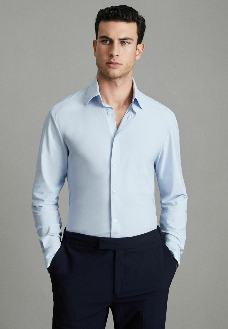 Hellblaues Langarmhemd mit Kragen, ausgestattet mit vorderen Knöpfen und einer glatten, eleganten Textur, kombiniert mit dunkelblauen Hosen.