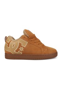 Brune semskede sneakers med polstret krave, stort beige DC-logo på siden, snørebånd foran og flad gummisål med "DCSHOECOUSA" branding.