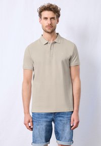 Beige poloko s krátkým rukávem a dvouknoflíkovou légou, v kombinaci s ohrnutými denimovými šortkami. Hladká textura látky, logo na prsou.