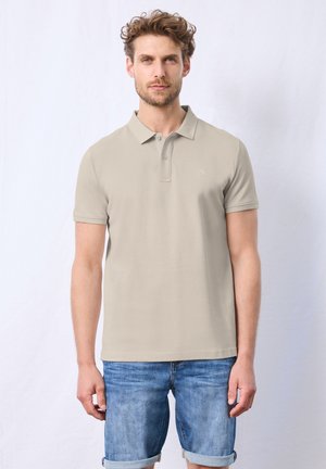 Polo beige a maniche corte con patta a due bottoni, abbinato a pantaloni corti in denim arrotolati. Tessuto liscio, logo sul petto.