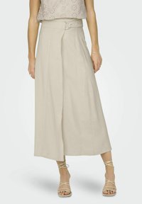 Beige, fließender A-Linien-Rock mit einem Frontwickel, einem Gürtel mit einer runden silbernen Schnalle und einer glatten Textur, kombiniert mit Riemchensandalen.