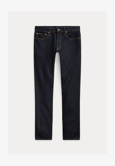 Tumedassinised kitsad teksad viie tasku, nööp-kinnituse ja kontrastõmblustega, tasapinnal heledal taustal.