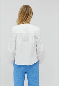 Blusa bianca con maniche a sbuffo, caratterizzata da uno scollo arricciato. Abbinata a pantaloni blu con texture. Design semplice e pulito.
