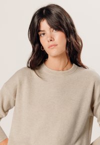 Beige gebreide trui met een ronde halslijn en afhangende schouders; zachte textuur en relaxte pasvorm; minimalistisch ontwerp zonder patronen.