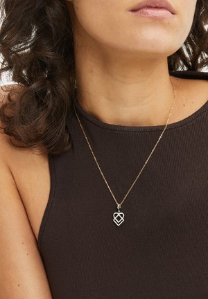 Gold-tone necklace featuring a double-heart pendant, attached to a delicate chain. The background shows a dark brown, ribbed fabric.