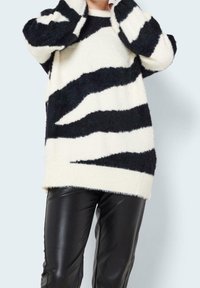 Czarnobiały, prążkowany, miękki sweter z dzianiny z długimi rękawami, zestawiony z błyszczącymi czarnymi spodniami z imitacji skóry. Sweter ma luźny krój.