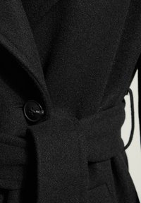 Schwarzer Wollmantel aus strukturiertem Stoff mit einem großen Knopfverschluss und einem Taillengürtel für eine verstellbare Passform.