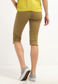 Béžové capri kalhoty se slim fit střihem, které mají dvě zadní kapsy a zkrácený design, doplněné o světle šedé slip-on boty.