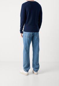 Maglietta a maniche lunghe navy con polsini e orlo a costine, abbinata a jeans azzurri chiari. L'outfit è completato da sneakers bianche, visto da dietro.