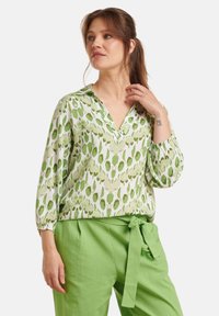 Green patterned blouse in lightweight fabric, featuring a V-neckline and three-quarter sleeves, paired with solid green paper-bag waist trousers.