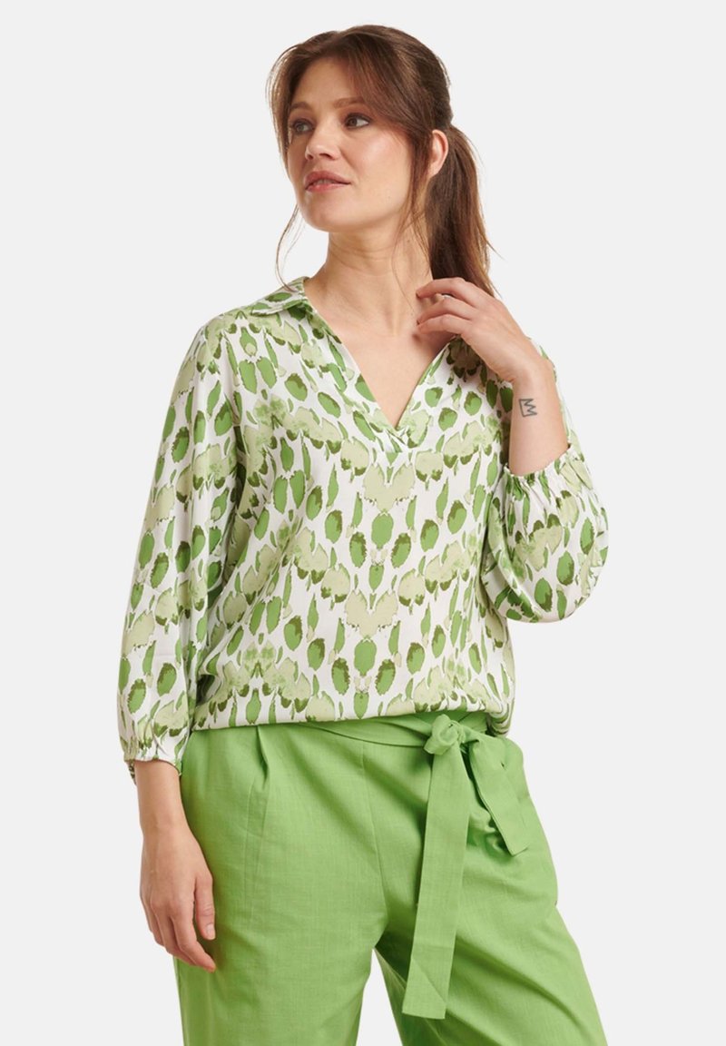 Green patterned blouse in lightweight fabric, featuring a V-neckline and three-quarter sleeves, paired with solid green paper-bag waist trousers.